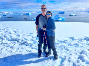 Dana and Chuck wearing fleece tops and rain pants, standing in Antarctic snow with sunglasses.